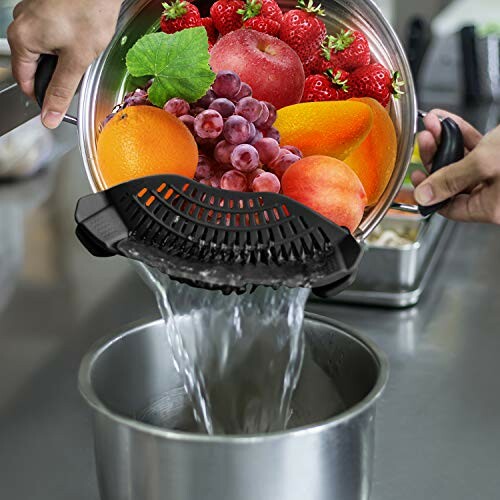 Person using a strainer to drain water from a pot of mixed fruits.