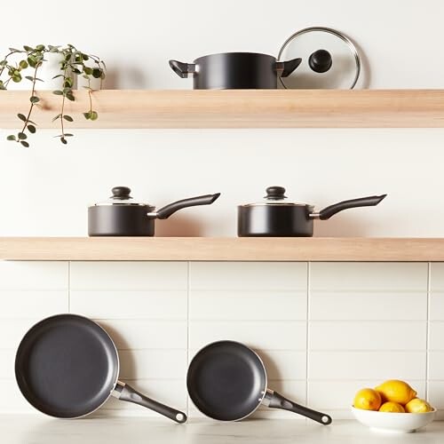 Black cookware set on wooden shelves with lemons and greenery.