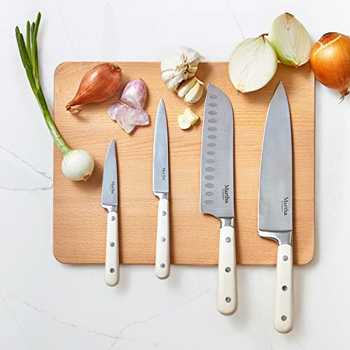 Set of kitchen knives on a wooden cutting board with onions and garlic.