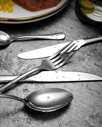 Assorted silverware on a wet surface with a plate nearby.