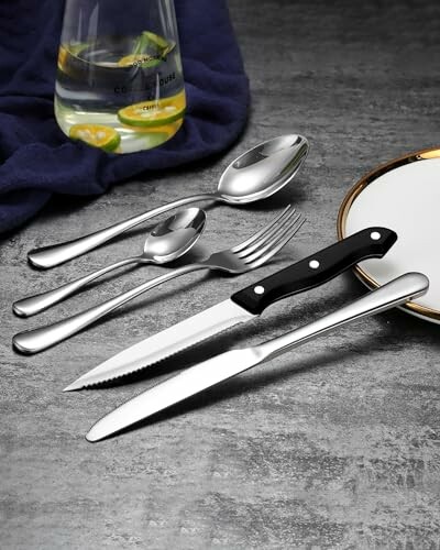 Silverware set with knife, fork, spoons, and drink on table.